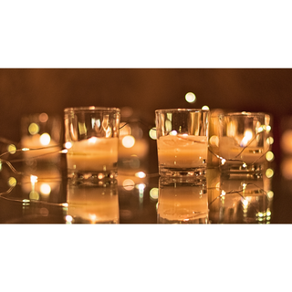 half used lit candles in glass vessel with fairy lights strewn about